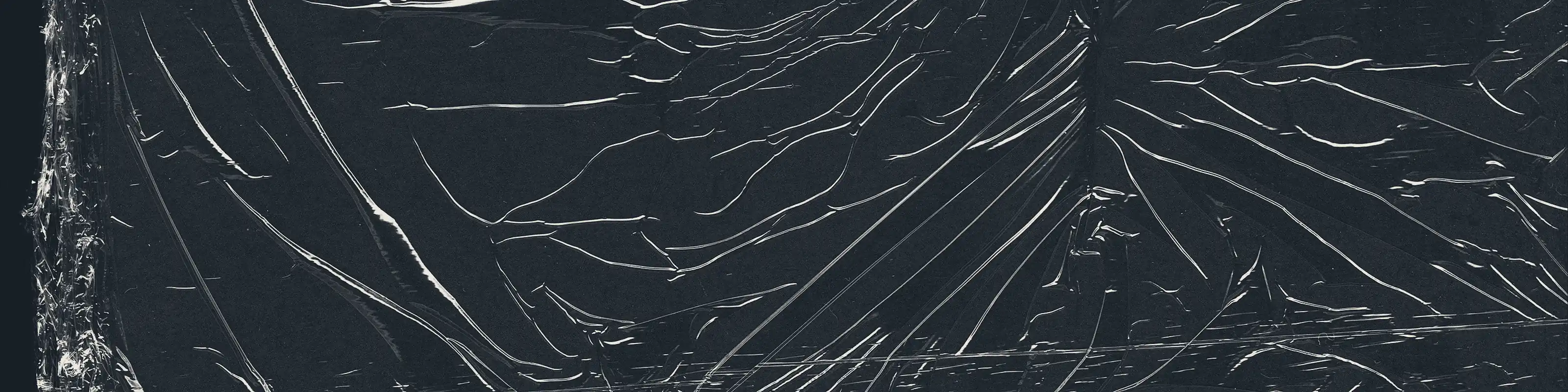 A sheet of polymer film drawn tight over a rectangular form and photographed close in: the lap edge of a second course runs down the left, and fine pull creases converge on a tension point at the right.