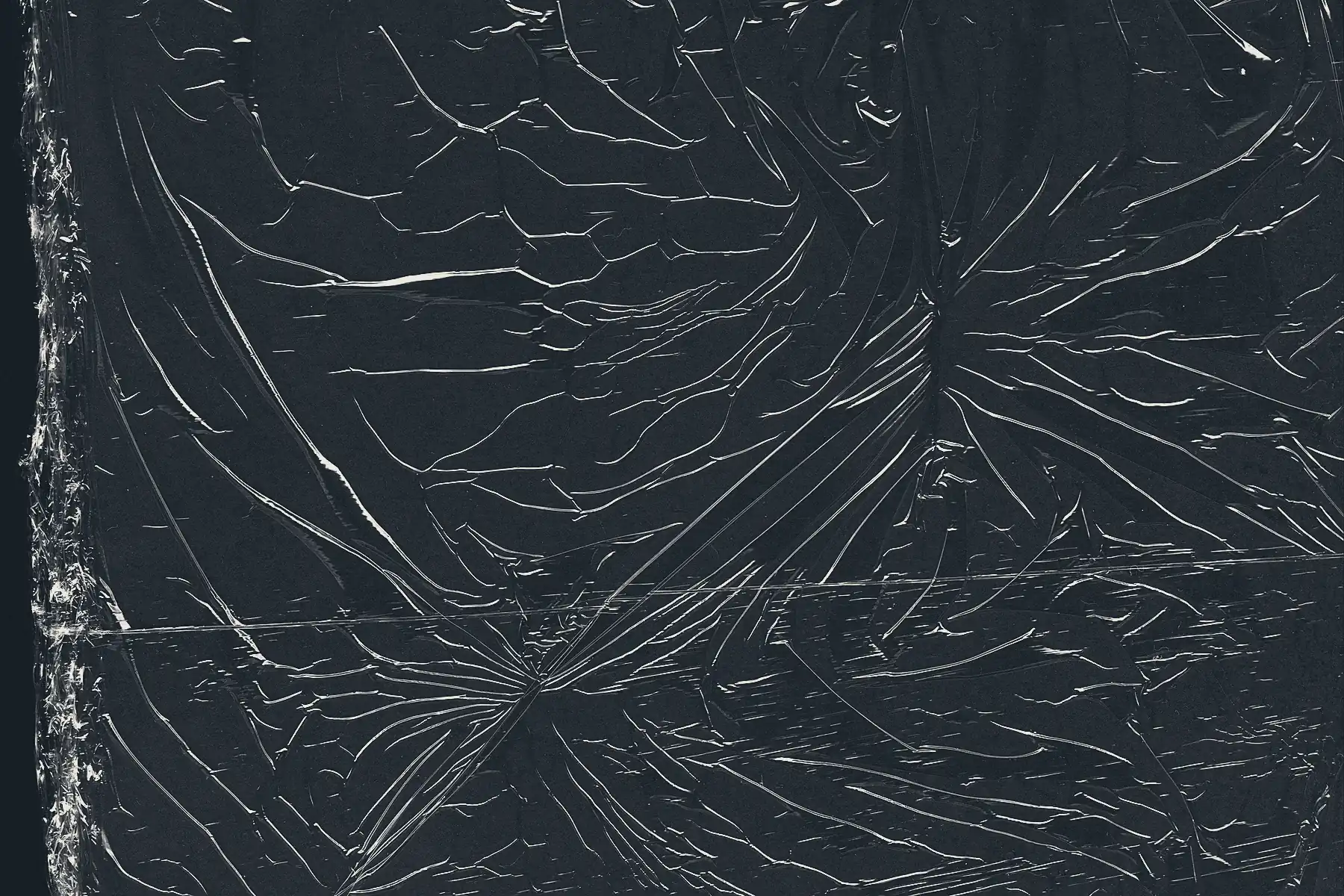 A sheet of polymer film drawn tight over a rectangular form and photographed close in: the lap edge of a second course runs down the left, and fine pull creases converge on a tension point at the right.